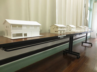 長机の上に長野工業高等専門学校5年生の作品「蔵の町並みの景観に配慮した二世帯店舗併用住宅」の模型が等間隔で置かれ展示されている写真