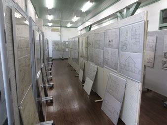 展示用パネルに信州大学工学部2年生が作成した「住宅の設計」図が設置され、人が見学出来る間隔を開けて縦3列に並んでいる作品展示会場の写真