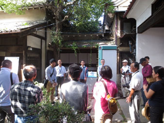 木漏れ日がさす建物と建物の間の敷地に、丸い円になって話をしている参加者達の写真