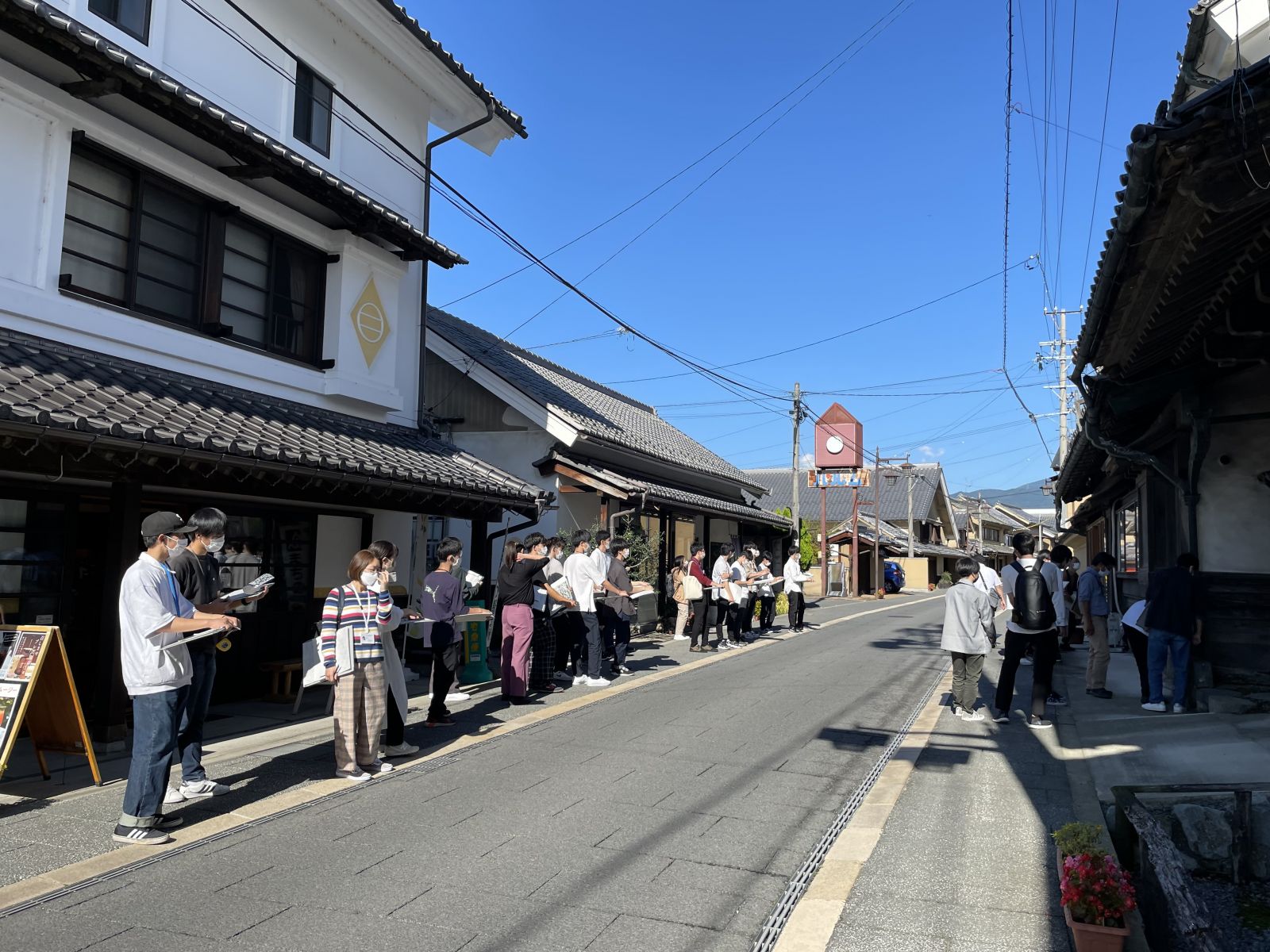 建物が立ち並ぶ道路沿いに、横一列に並んでいる学生たちの授業風景を写した写真