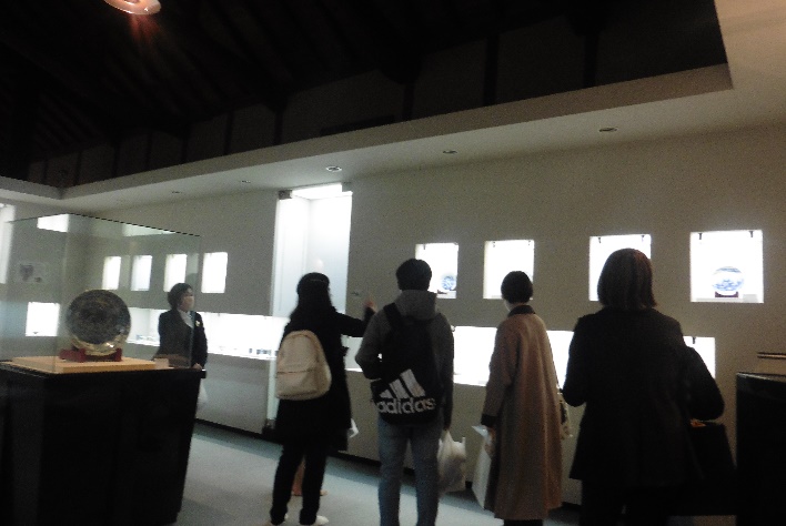 ライトアップされたお皿などの展示物を見ている大学生たちの写真