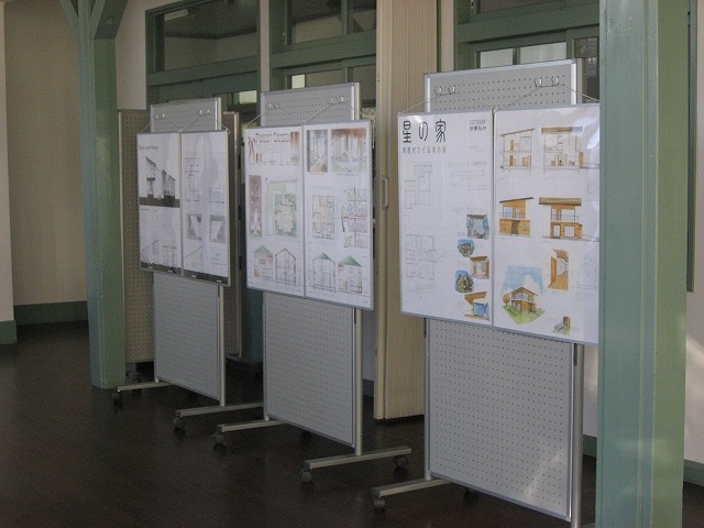 横一列に等間隔に並べられた3枚の長方形の展示パネルに、信州大学工学部2年生が作成した「住宅の設計」が2枚ずつ展示されている写真