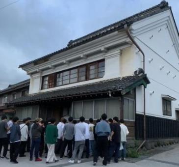 街区の再生授業の様子写真。蔵造りの家の前で説明を聞く生徒たちの様子。