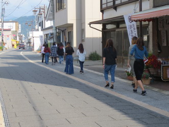 石畳の道路の右側の建物沿いにある歩道内を、蔵の町並みの視察をしながら奥に向かって歩いていく女学生たちの後ろ姿の写真