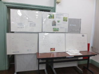 作品が設置された展示パネルと長机の上に、長野工業高等専門学校5年生が作成した「多世代が蔵の街で共存する集合住宅の設計」と「あたりまえをReスタート」の作品が設置された展示風景の写真