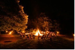 夜にキャンプファイヤーを大勢の人たちが囲んでいる。