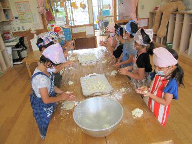 数名の園児が机にあつまり、机の上にある生地をちぎって丸めてお団子を作っている様子。