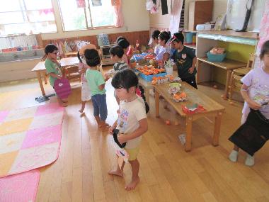 保育室内で、机の上に折り紙で作った卵や、卵入れがたくさんあります。机を隔ててお店屋さんごっこをやっている園児の様子。