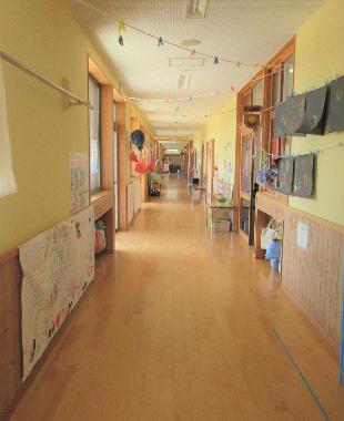 奥まで一直線に続く園舎内の木の廊下。右側に保育室、左側に園庭がある。廊下の両サイドの壁には園児の作品が飾られている。