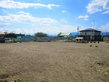 井上保育園の広い園庭写真。奥には木製の小屋や、遊具が小さく見えます。