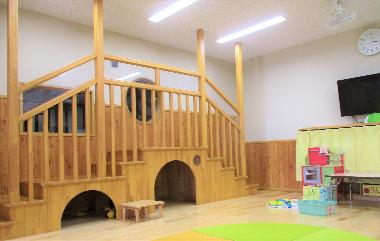 給食室の壁面の高い場所に丸や四角の大きな窓があります。その高さに合わせて木製の高台が作られ、高台の下は園児2,3名が入れる小さな部屋になっています。