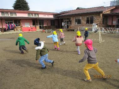 冬。ジャンバーやニット帽子をかぶる園児が、井上保育園の園庭で元気にサッカーをして遊ぶ様子。右側には小さなサッカーゴール。園庭の奥には園舎。