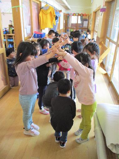 誕生日会の写真。園内の廊下を異年齢の園児たちが二列に並び、両手を上にあげてトンネルを作り、お誕生日の子がそのなかをくぐっていく。