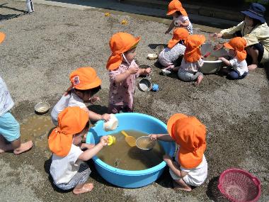 須坂保育園どろんこあそび。園庭の砂場に、大きなプラスチック洗濯おけに水を汲み、泥んこ遊びをする園児たち。