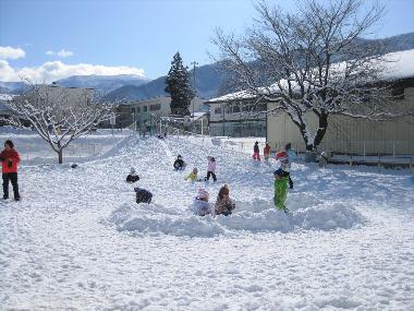 季節は冬で一面は雪景色。高甫小学校とつながる園庭の坂道にも雪が積もり、スキーウエアを着た園児が青空の下でそり遊びなど、雪遊びを楽しむ様子。