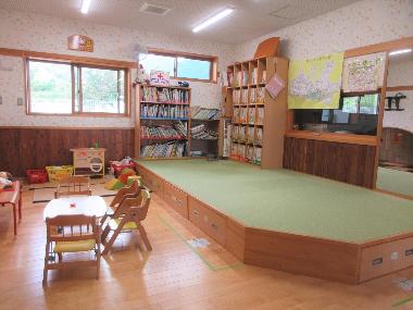 絵本を読むスペースは3畳くらいで絨毯張りで一段高くなっています。その前には机といす、奥には畳のスペースがあります。一段高くなった絨毯の壁側には絵本や紙芝居が置かれ、園児は自由に本を読めるようになっています。