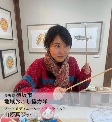地域おこし協力隊山際真奈さんの写真。両手に編み針を持ってポーズをとっています。