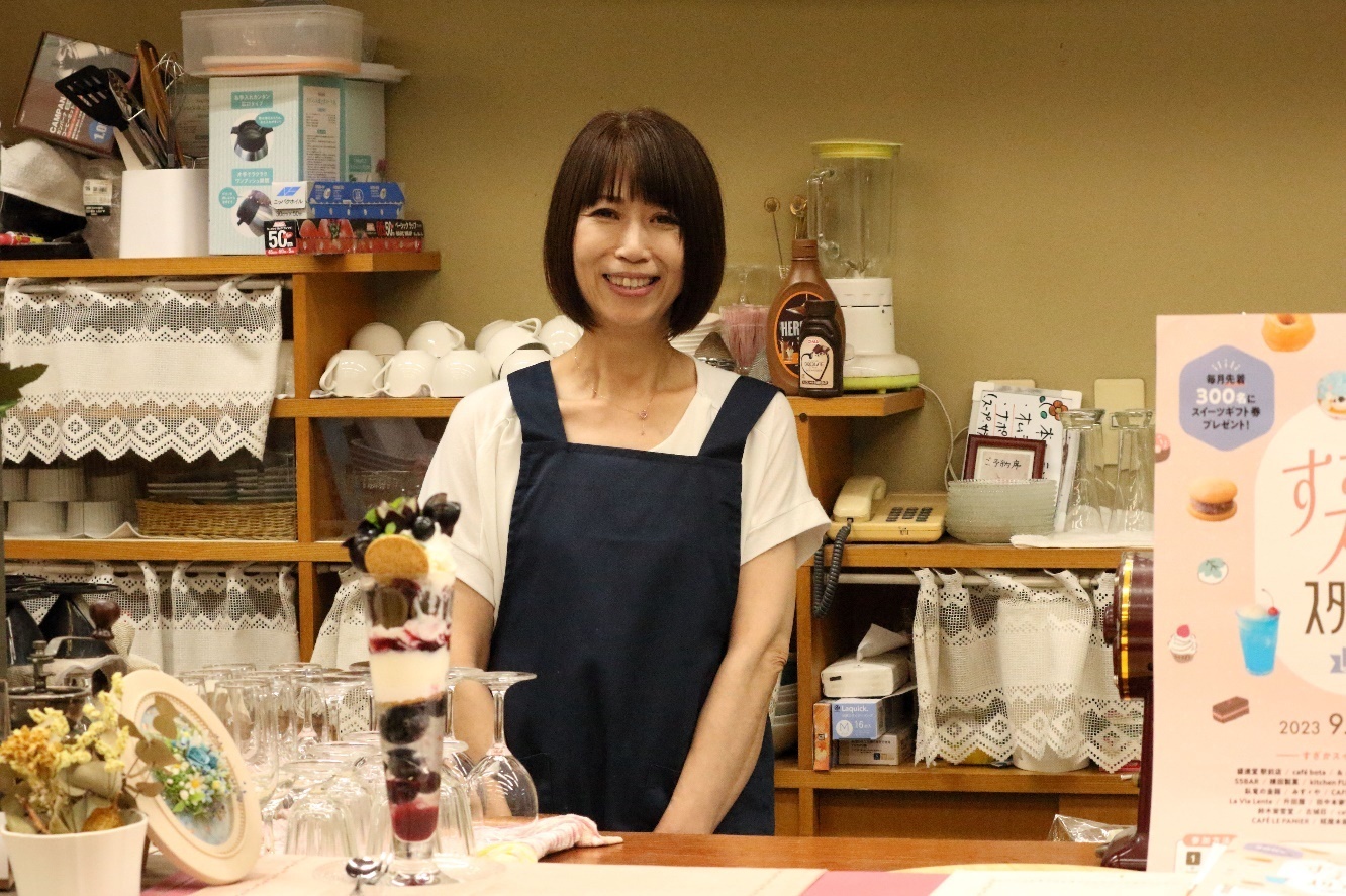 店のカウンター内でほほ笑むエプロン姿の長田良子さんの写真