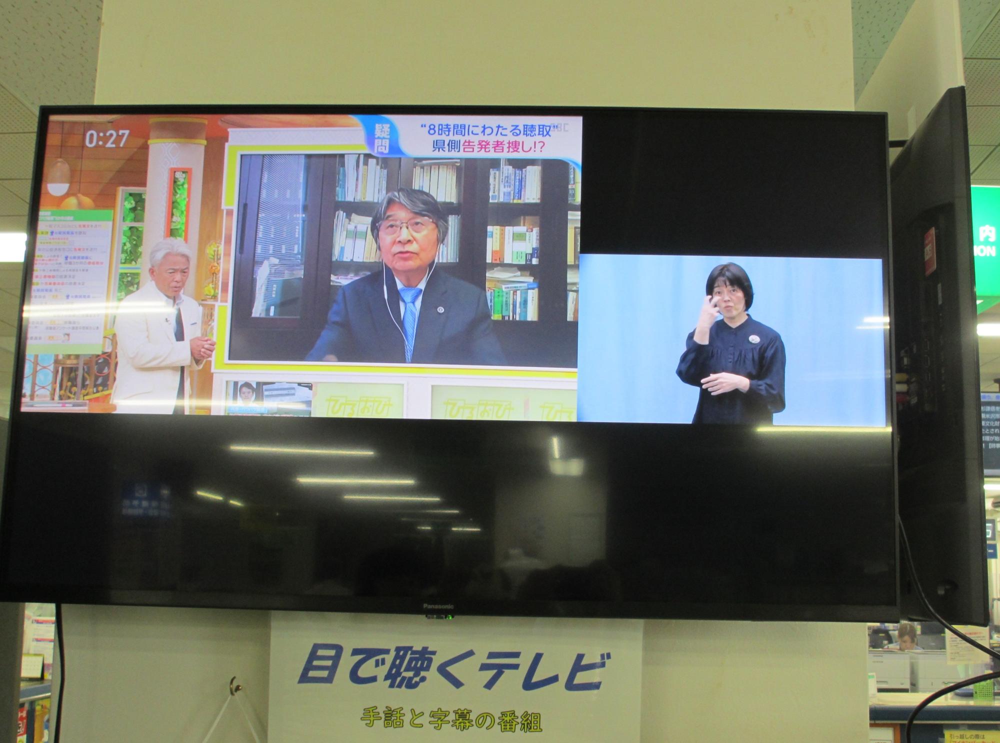 目で聴くテレビ（ニュース映像）、画面左側にニュース番組、右側に手話通訳者が手話をしている画面が出ている。