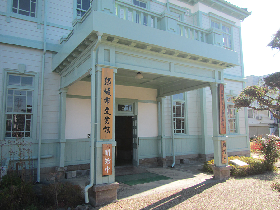青い外壁と白い窓枠を持つ木造洋風建築の正面玄関ポーチを写した写真で、「須坂市文書館」と「開館中」の縦看板が掲げられた柱があり、歴史を感じさせる建物である写真