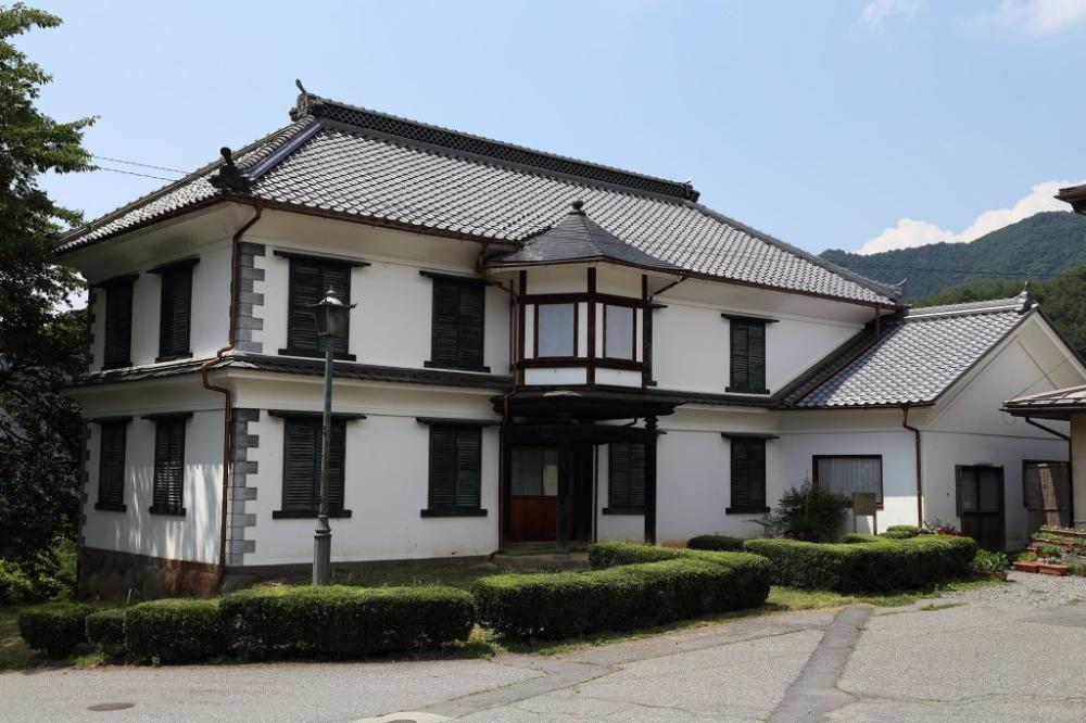 白壁に黒い瓦屋根が乗った洋風と和風が融合した旧園里学校の校舎が、青空の下に建っている写真